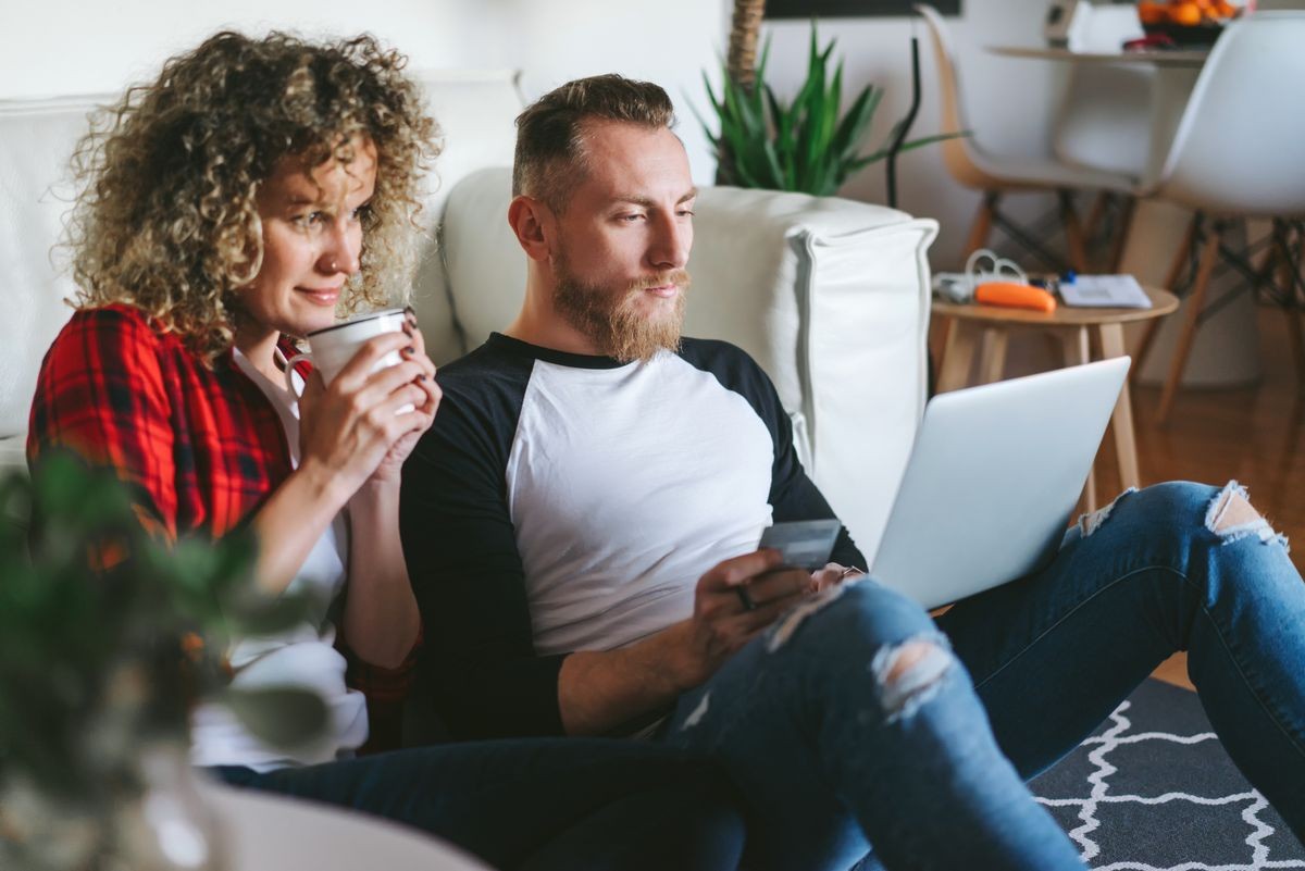 Happy young casually dressed hipster couple spending time together at home doing online shopping.